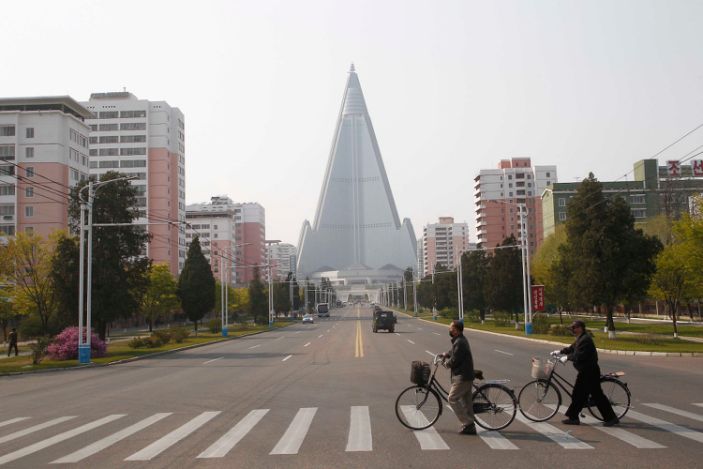 أشخاص يرتدون أقنعة الوجه يعبرون طريقًا أمام فندق Ryugyong في بيونغ يانغ ، كوريا الشمالية الثلاثاء 28 أبريل 2020.